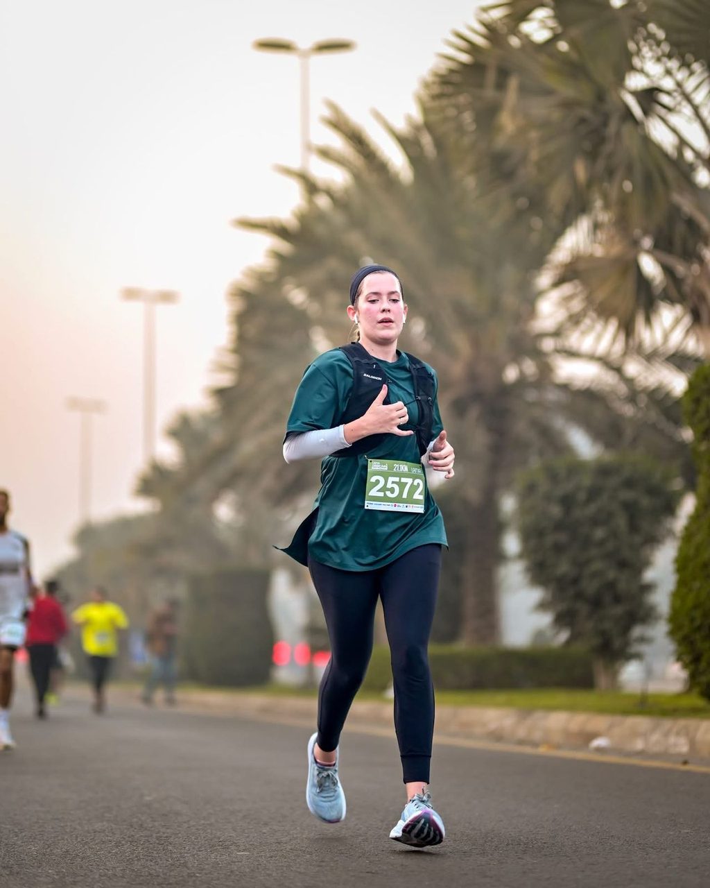 A woman in a green top running along a palm-lined road